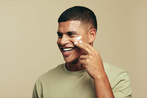 Skin care for men: Youthful male applies beauty cream to his face