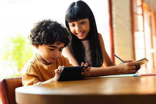 Young siblings spending time together at home using technology and studying