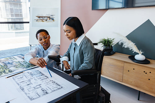 Two women collaborating on architectural plans in an office setting