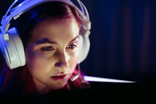 Young female gamer playing a video game at night, wearing headphones