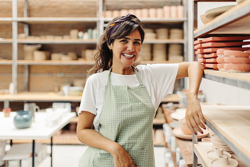 Happy female potter smiling at the camera in her shop