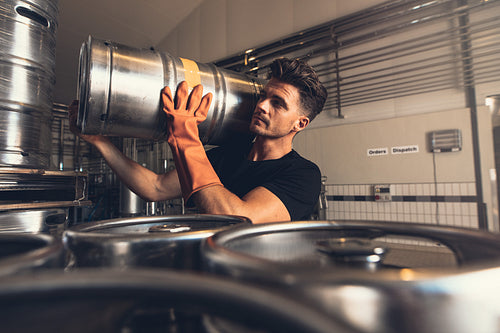 Brewer carrying metal beer barrel at brewery factory