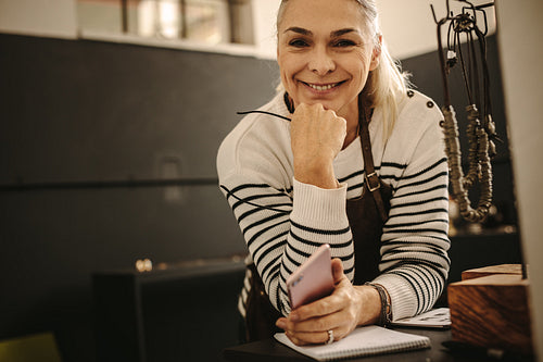 Smiling female jeweler leaning to desk