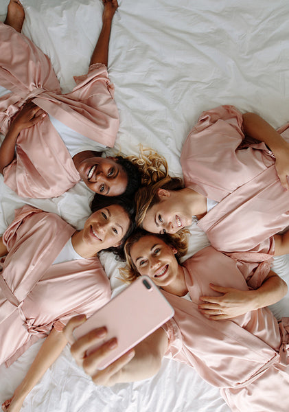 Bride taking selfie with bridesmaids while lying on bed