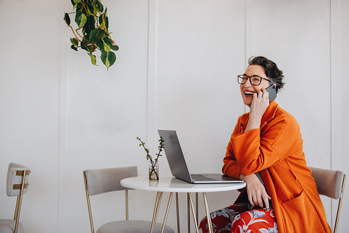 Happy mature businesswoman speaking on a phone call while working in a cafe
