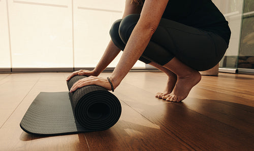 Unrecognizable senior woman rolling up an exercise mat at home