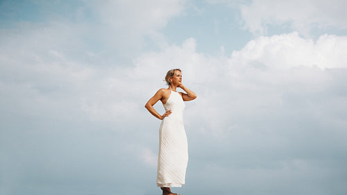 Woman in white dress standing against a cloudy sky outdoors