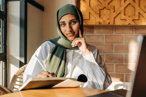Female student with a headscarf looking at the camera in a cafe