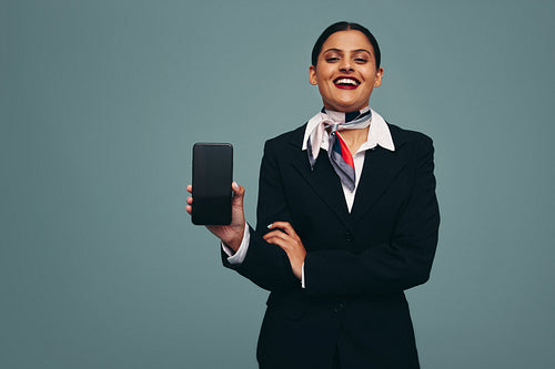 Young flight attendant holding up a smartphone in a studio