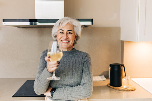 Happy senior woman holding a glass of sparkling wine at home
