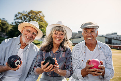 Elderly men and a woman sitting outdoors holding boules