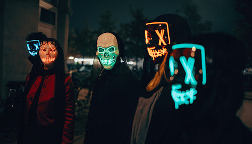 Group in neon masks gathering outdoors during nighttime for halloween
