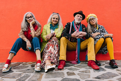 Carefree elderly friends sitting against a red wall
