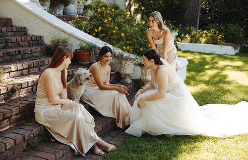 Bride chatting with bridesmaids on garden steps during a sunny wedding day