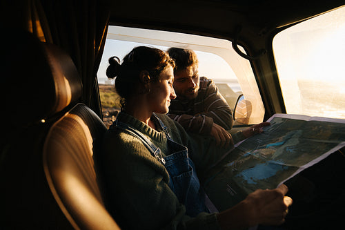 Couple in a car reading a map during sunset on a road trip
