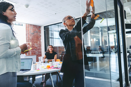 Creative businesswomen sticking adhesive notes to a glass wall