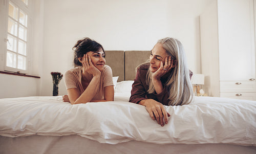 Happy mother and daughter talking while resting on bed