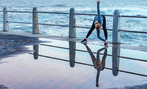 Reflection on wet road of woman doing stretches