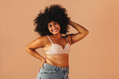 Body positive woman smiling at the camera while wearing a bra and jeans