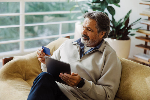 Senior man shops online with tablet and credit card at home