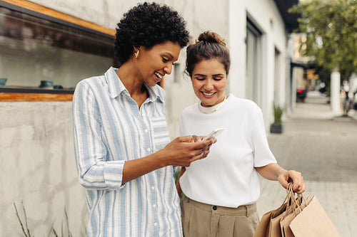 Two happy young women e-hailing a ride after shopping in the city