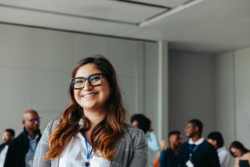 Smiling professional woman at a business conference with colleagues in the background