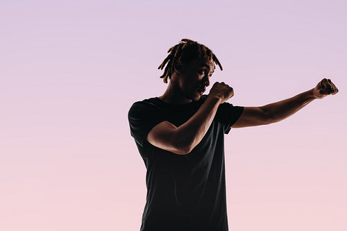 Young martial artist practicing boxing in a striking silhouette against a pink background