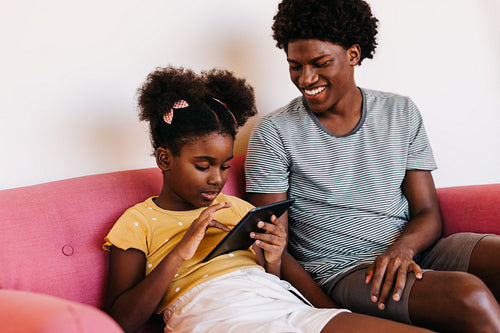 Brother and sister sharing a tablet, enjoying screen time together on the sofa