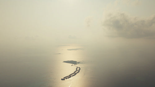 Aerial drone view of a beautiful tropical island resort with overwater bungalows reflecting sun