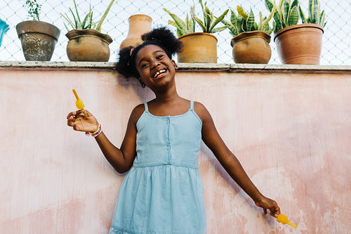 Cheerful afro-haired girl enjoying ice lollies outdoors at home