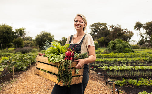 Happy female farmer holding a box with fresh produce