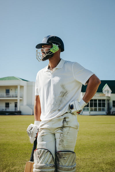 Male cricket player in uniform with bat standing on cricket field