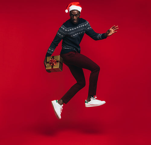 Stylish man jumping with christmas present