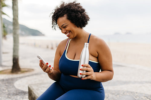 Healthy summer workout by the ocean: Woman using her phone to track fitness progress