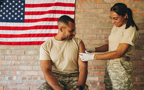Female medic applying a band aid to a soldier's arm after vaccin