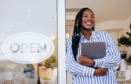 Successful small business owner standing next to an open sign in her new cafe