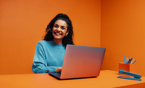 Cheerful woman in an online meeting using a laptop, wearing a headset. Smiling and engaged online employee.