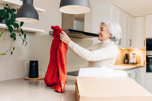 Satisfied elderly woman unpacking a clothing delivery at home