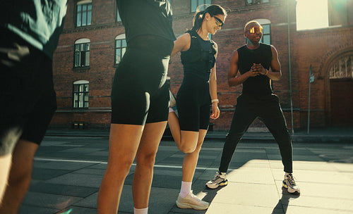 Running group warm up with young adults stretching outdoors before a city workout