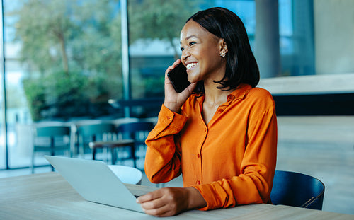 Smiling woman using phone while working on laptop in modern office