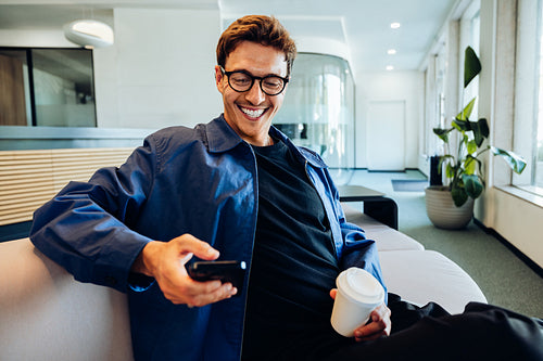 Man with coffee and phone in office lounge