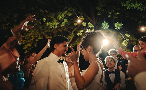 Outdoor wedding celebration with bride, groom, and guests enjoying under string lights