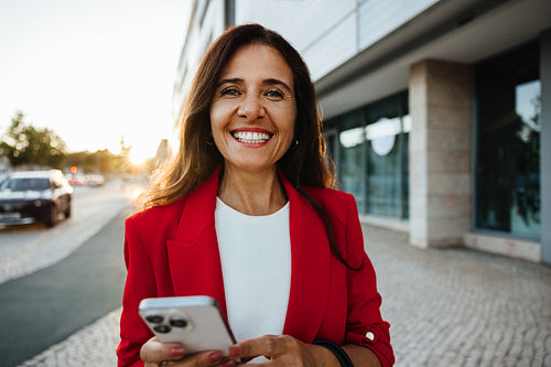 Smiling woman outdoors holding a phone during a sunny day