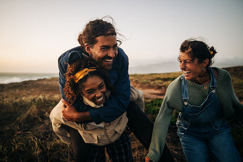 Friends share a joyful moment on a windy coast as one carries another and everyone smiles
