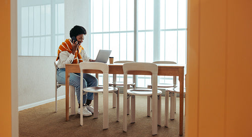 African woman making a business call while working on a laptop in an office