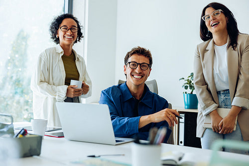 Three colleagues laugh during a desk meeting
