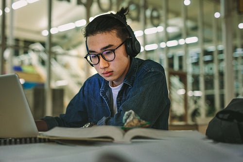 Student with headphones studying on the laptop at library