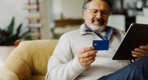 Senior man shops online with a credit card and tablet