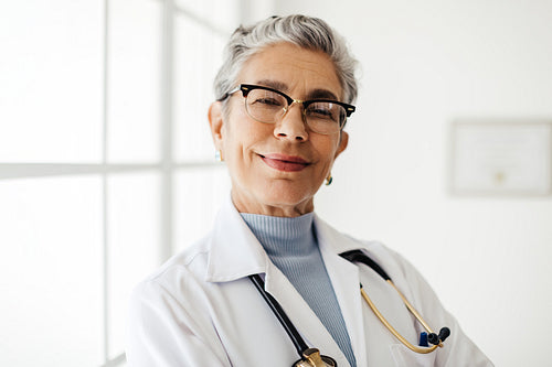 Confident and experienced: Mature doctor stands in her office looking at the camera