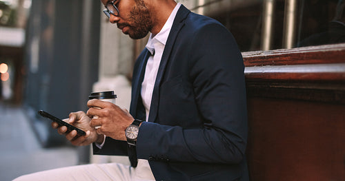 Businessman sitting outside with coffee using phone
